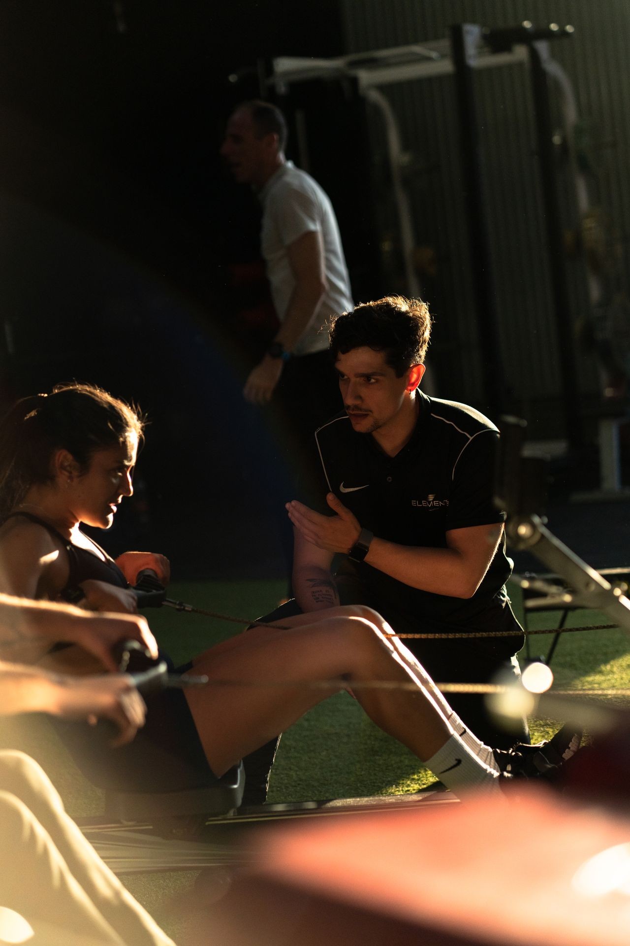 Trainer coaching a person on a rowing machine in a gym with dim lighting.